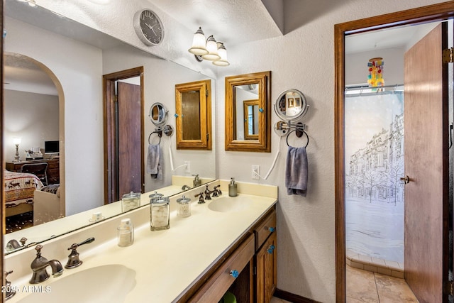 ensuite bathroom with double vanity, ensuite bath, a textured wall, and a sink