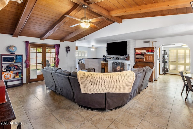 living area with visible vents, lofted ceiling with beams, french doors, a fireplace, and arched walkways