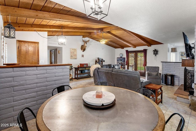 dining space with a brick fireplace, lofted ceiling with beams, ceiling fan with notable chandelier, french doors, and wooden ceiling