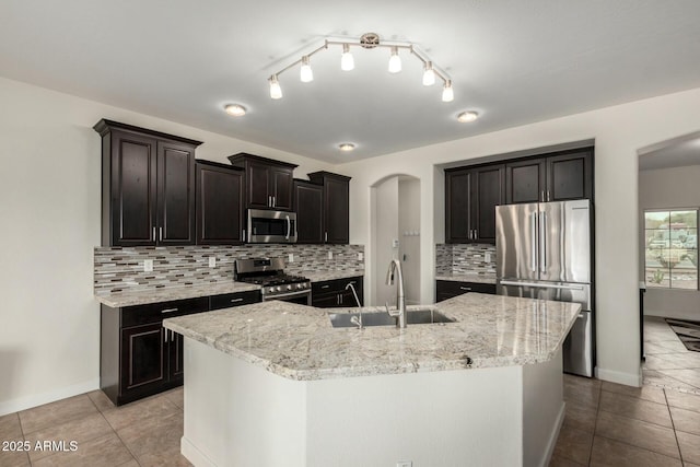 kitchen with appliances with stainless steel finishes, a kitchen island with sink, a sink, and light tile patterned floors