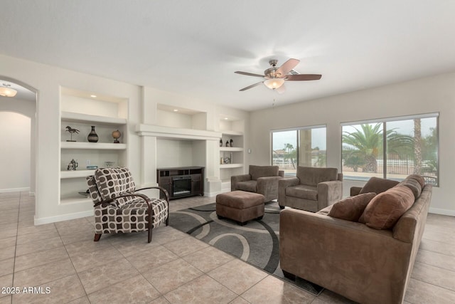 living room featuring light tile patterned floors, baseboards, arched walkways, built in shelves, and a fireplace