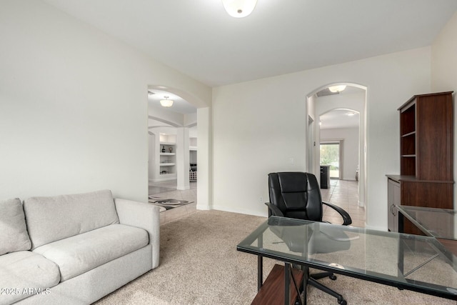 carpeted office space featuring built in shelves and arched walkways