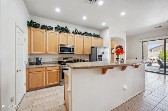 4414 W Monte Way, Laveen, AZ 85339 - kitchen featuring stainless steel appliances, light brown cabinets, light tile patterned flooring, arched walkways, and a kitchen bar