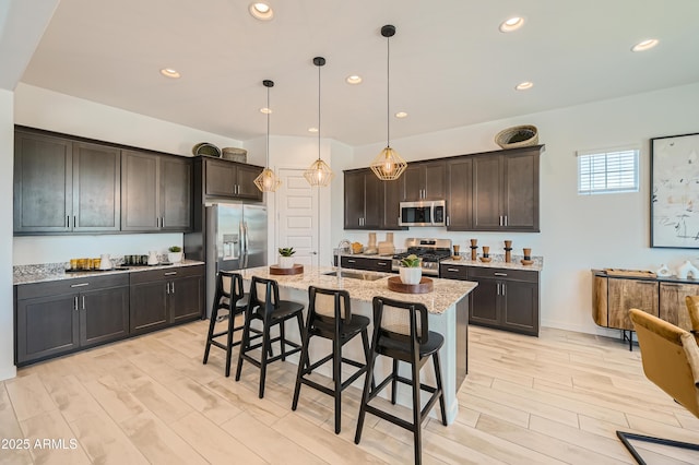 kitchen with a sink, light stone counters, a kitchen breakfast bar, stainless steel appliances, and dark brown cabinetry