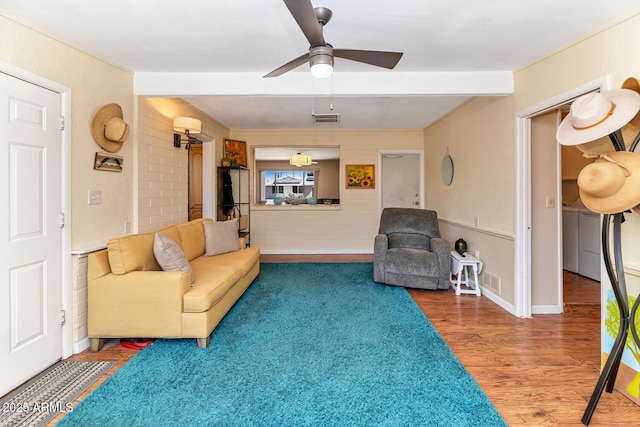 living room with ceiling fan, wood finished floors, visible vents, baseboards, and beam ceiling