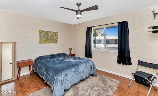 bedroom with ceiling fan, brick wall, wood finished floors, and baseboards