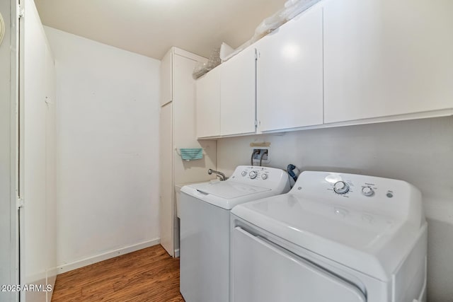 clothes washing area featuring cabinet space, washing machine and dryer, baseboards, and dark wood finished floors