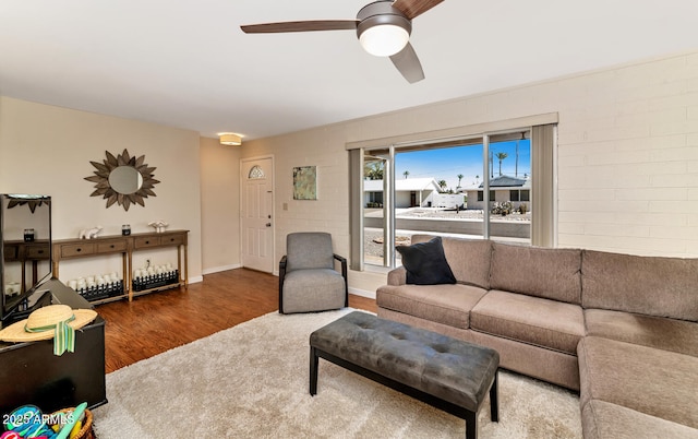 living area with ceiling fan, brick wall, dark wood-style flooring, and baseboards