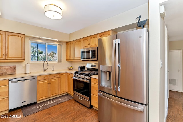 kitchen featuring stainless steel appliances, a sink, wood finished floors, visible vents, and light countertops