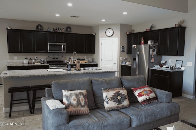 kitchen featuring light stone countertops, stainless steel appliances, and an island with sink