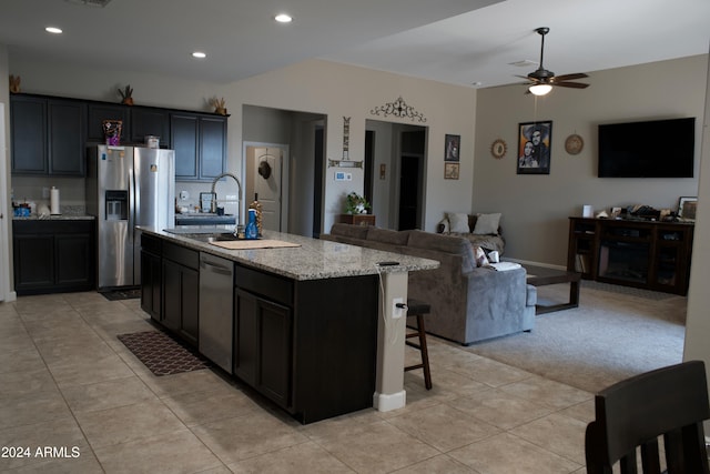 kitchen with ceiling fan, light stone countertops, an island with sink, light tile patterned floors, and appliances with stainless steel finishes