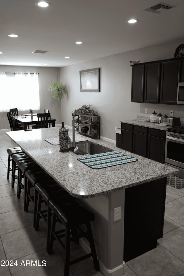 kitchen with a breakfast bar area, light stone counters, an island with sink, and stainless steel appliances