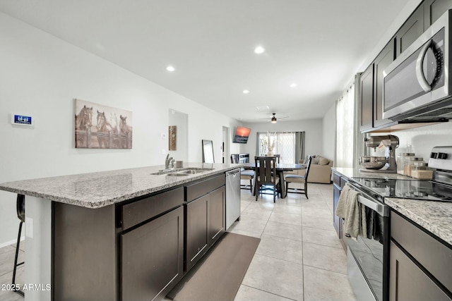 kitchen with light tile patterned floors, light stone countertops, a kitchen island with sink, a sink, and appliances with stainless steel finishes