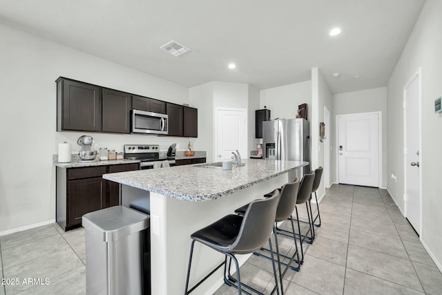 kitchen featuring light tile patterned floors, visible vents, a sink, stainless steel appliances, and a kitchen breakfast bar