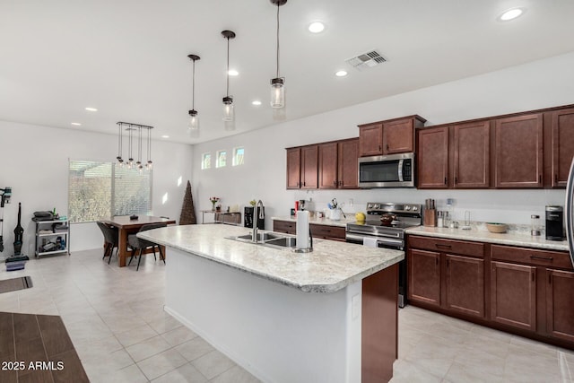 kitchen with light tile patterned flooring, appliances with stainless steel finishes, decorative light fixtures, sink, and a center island with sink