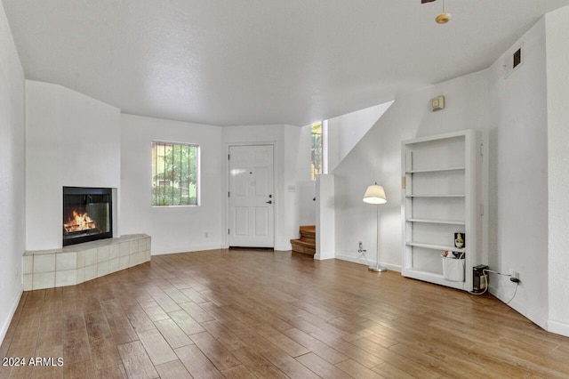 unfurnished living room with wood-type flooring, built in shelves, and a tile fireplace