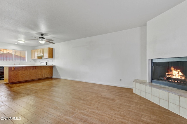 unfurnished living room featuring light hardwood / wood-style flooring, a fireplace, a textured ceiling, ceiling fan, and sink