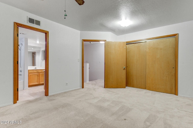 unfurnished bedroom featuring a textured ceiling, ceiling fan, ensuite bath, a closet, and light colored carpet