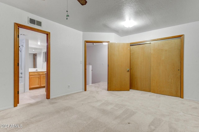 unfurnished bedroom with connected bathroom, light colored carpet, ceiling fan, a textured ceiling, and a closet