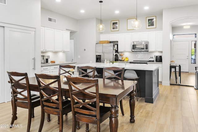 kitchen featuring a kitchen bar, light wood-style floors, arched walkways, stainless steel appliances, and a kitchen island with sink