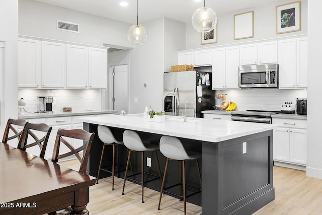 kitchen featuring visible vents, a breakfast bar, an island with sink, light wood-type flooring, and appliances with stainless steel finishes