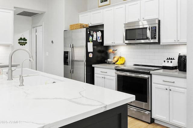 kitchen featuring light wood-type flooring, a sink, backsplash, appliances with stainless steel finishes, and white cabinets