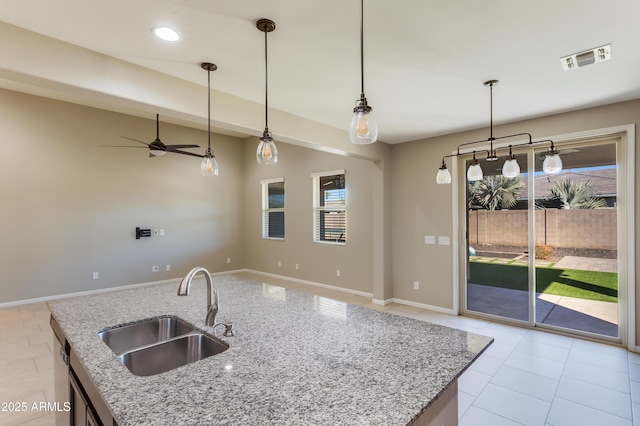 kitchen with hanging light fixtures, light stone countertops, sink, and a kitchen island with sink