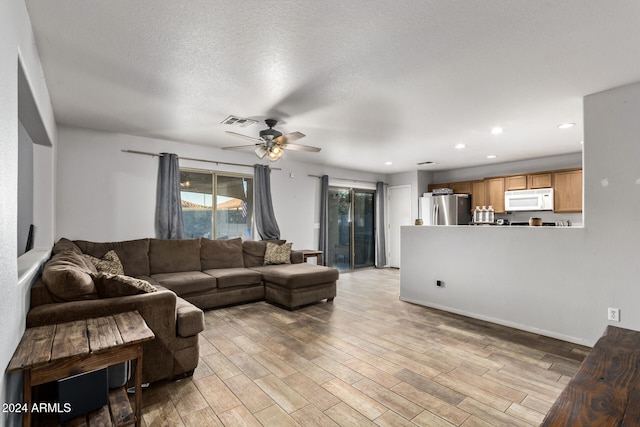 living room featuring ceiling fan, light hardwood / wood-style floors, and a textured ceiling