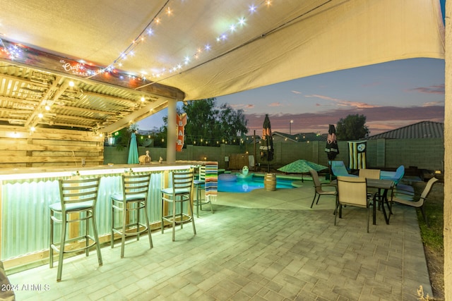 patio terrace at dusk with a bar, a pergola, and a swimming pool