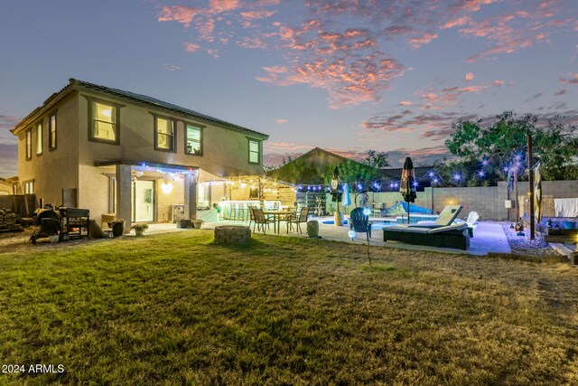 back house at dusk featuring a lawn and a swimming pool