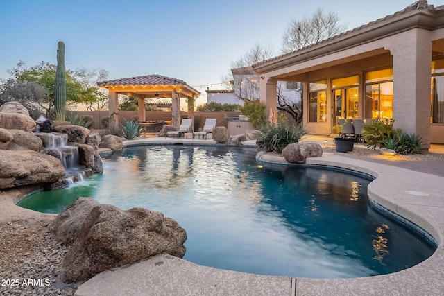 pool at dusk with a gazebo, pool water feature, and a patio