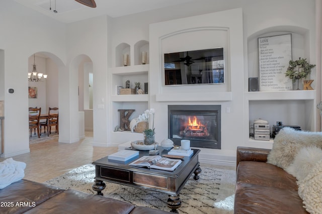 living room featuring ceiling fan with notable chandelier, built in shelves, and light tile patterned flooring