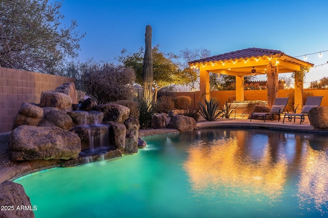 pool at dusk featuring pool water feature and a gazebo