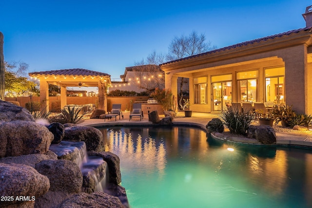 pool at dusk featuring an outdoor kitchen and a patio