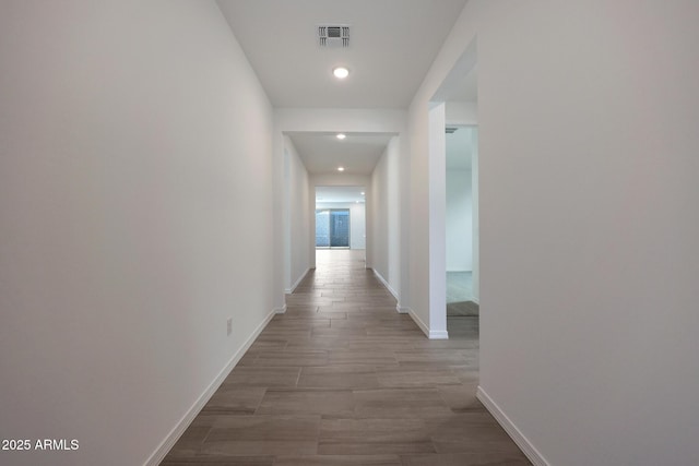 hall with light wood finished floors, visible vents, and baseboards