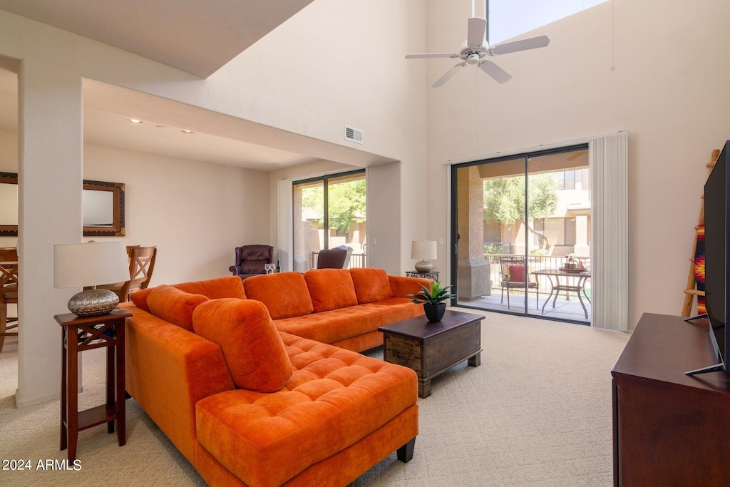 carpeted living room featuring ceiling fan and a high ceiling