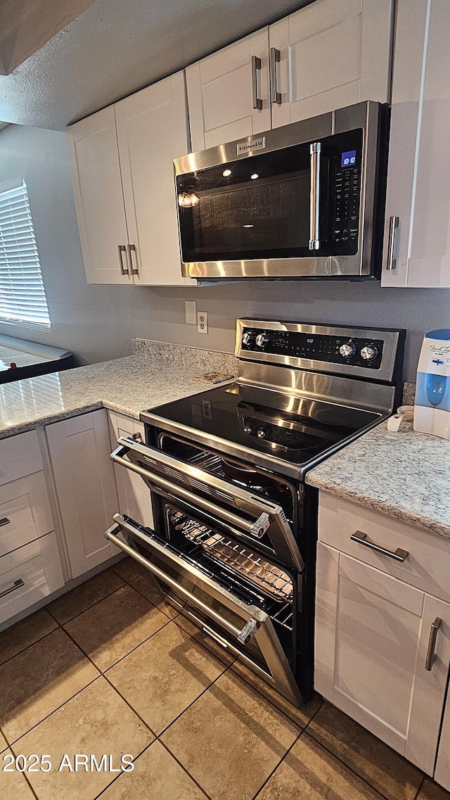 5751 W Muriel Dr, Glendale, AZ 85308 - kitchen featuring stainless steel microwave, range with electric cooktop, tile patterned flooring, white cabinetry, and light stone countertops