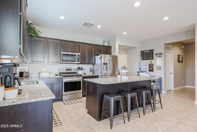 kitchen featuring light stone counters, light tile patterned floors, a kitchen island, and appliances with stainless steel finishes