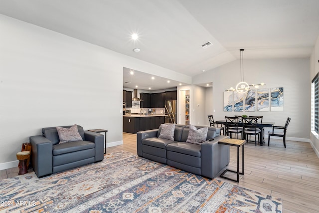 living room with a chandelier, light hardwood / wood-style floors, and lofted ceiling