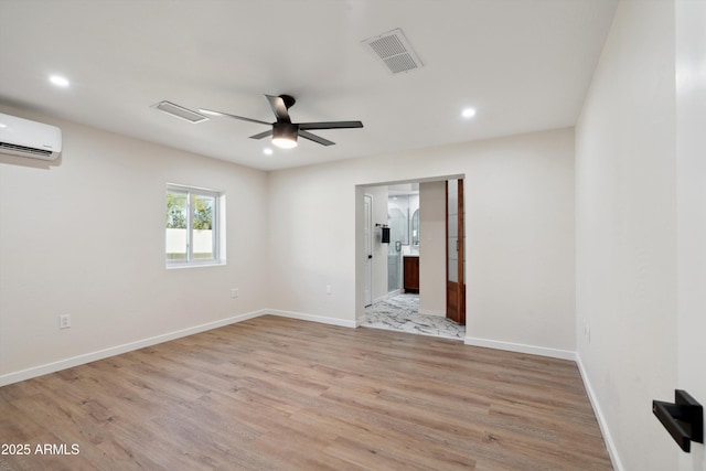 spare room with ceiling fan, a wall unit AC, visible vents, baseboards, and light wood finished floors