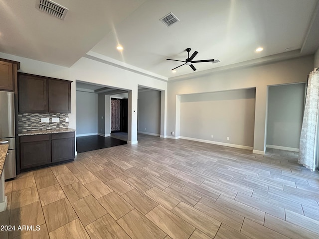 kitchen featuring stainless steel fridge, tasteful backsplash, ceiling fan, light stone countertops, and dark brown cabinetry