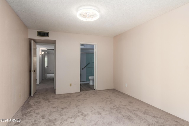 unfurnished bedroom featuring ensuite bath, visible vents, carpet, and a textured ceiling