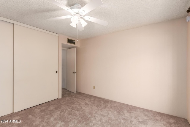 unfurnished bedroom featuring carpet, a textured ceiling, visible vents, a ceiling fan, and a closet
