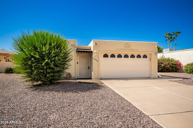 pueblo revival-style home featuring driveway, stucco siding, and an attached garage