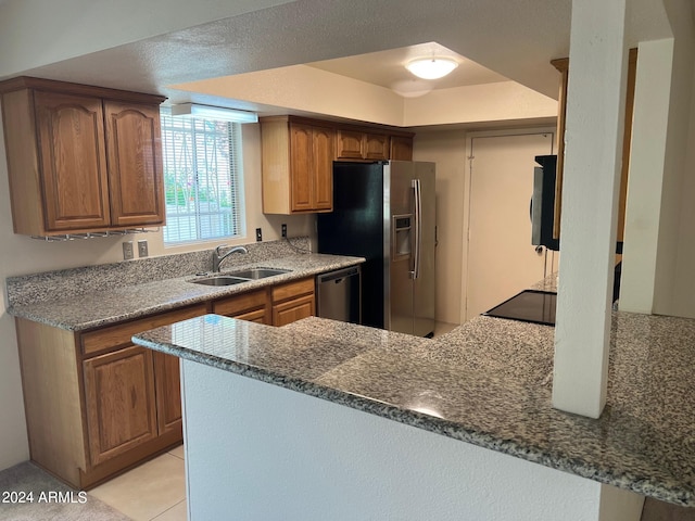 kitchen featuring stainless steel appliances, kitchen peninsula, sink, and dark stone counters