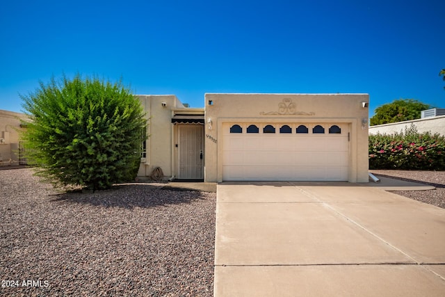 pueblo-style house featuring driveway, stucco siding, and an attached garage