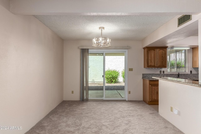 kitchen featuring visible vents, plenty of natural light, light carpet, brown cabinetry, and a notable chandelier