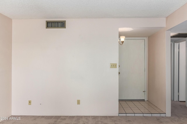 empty room featuring a textured ceiling, light colored carpet, and visible vents