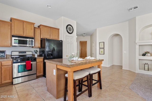 3026 W Silver Fox Way, Phoenix, AZ 85045 - kitchen featuring stainless steel appliances, light tile patterned floors, a kitchen bar, arched walkways, and a center island