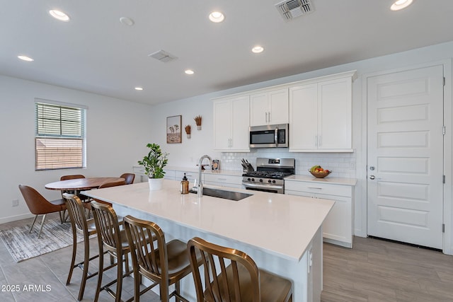 kitchen featuring visible vents, decorative backsplash, a kitchen breakfast bar, stainless steel appliances, and a sink